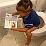 Jaisah is registered to the contest to win money with this photo: barefoot, bathroom, bathroom_rug, bathtub, blue_shirt, book, cabinet, candid, casual, child, curtain, indoor, multitasking, reading, sitting, tile_floor, toddler, toilet, top_knot, young_child