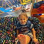 Jaisah is registered to the contest to win money with this photo: activity, carpet, child, couch, floor, foot, furniture, hair_tie, indoor, kids, numbers, person, play, playroom, shirt, shorts, smiling, toddler, toy, yellow_chairs