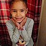 Myra is registered to the contest to win money with this photo: child, girl, smile, braids, pajamas, minnie_mouse, gray_clothing, plaid_background, hands_on_chin, indoors, cute, happy, portrait, young_child, colorful, patterned_background, long_sleeves, casual_wear, standing, playful