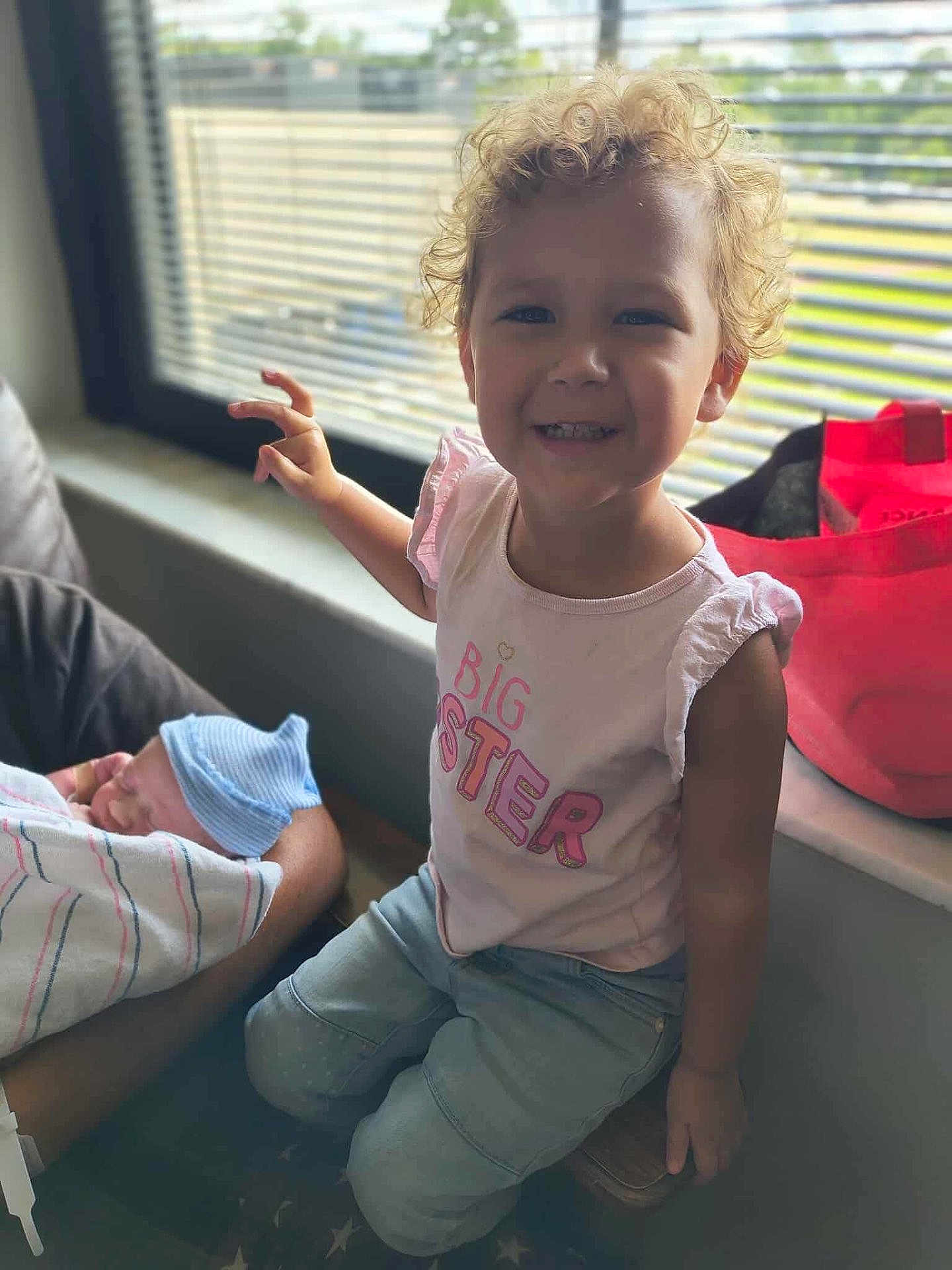 Bella joined the competition — help win amazing prizes! child, toddler, baby, newborn, curly_hair, smiling, sibling, big_sister_shirt, window, natural_light, indoor, person, clothing, blanket, hat, arm, seated, happy, family, love