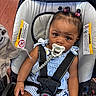 Royaltii is registered to the contest to win money with this photo: baby, child, car_seat, pacifier, hair_buns, beads, blue_striped_clothing, safety_harness, indoor, floor, wood_floor, infant, cute, looking_at_camera, seated, human, small_hands, expression, adorable, wearing