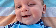 Archie is registered to the contest to win money with this photo: baby, child, smiling, face, blue_shirt, sailboats, striped_towel, outdoor, happy, cute, infant, portrait, clothing, person, head, skin, cheeks, eyes, mouth, expression