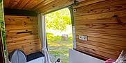 Pistache a rejoint le concours — aidez-le/la à gagner de superbes lots ! bed, bench, calico_cat, cat, cozy, curtain, flooring, greenery, interior, nature_outside, open_door, peaceful, pillow, pink_bedding, plant, shoes, sunlight, white_cabinet, wood_panels, wooden_cabin