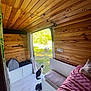 bed, bench, calico_cat, cat, cozy, curtain, flooring, greenery, interior, nature_outside, open_door, peaceful, pillow, pink_bedding, plant, shoes, sunlight, white_cabinet, wood_panels, wooden_cabin