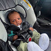 Reshawn is registered to the contest to win money with this photo: baby, car_seat, infant, hoodie, seatbelt, pacifier, clothing, car_interior, socks, green_pants, black_straps, sitting, child, serious_expression, safety, automobile, infant_care, cute, portrait, indoors