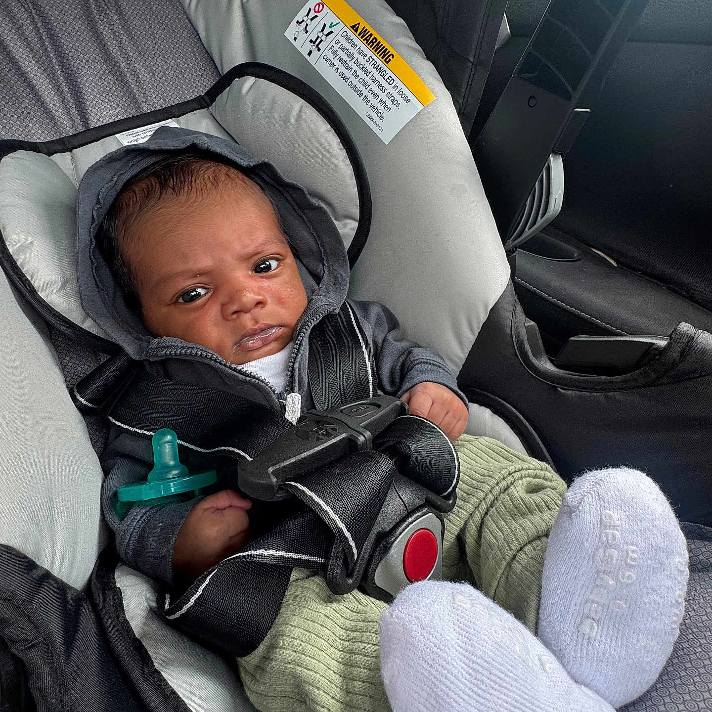 Reshawn is registered to the contest to win money with this photo: baby, car_seat, infant, hoodie, seatbelt, pacifier, clothing, car_interior, socks, green_pants, black_straps, sitting, child, serious_expression, safety, automobile, infant_care, cute, portrait, indoors