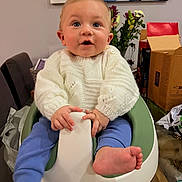 Rudy is registered to the contest to win money with this photo: baby, baby_seat, barefoot, blue_pants, cardboard_box, casual, child, curious, face, flowers, furniture, hands, head, home, indoor, infant, person, smiling, sweater, table