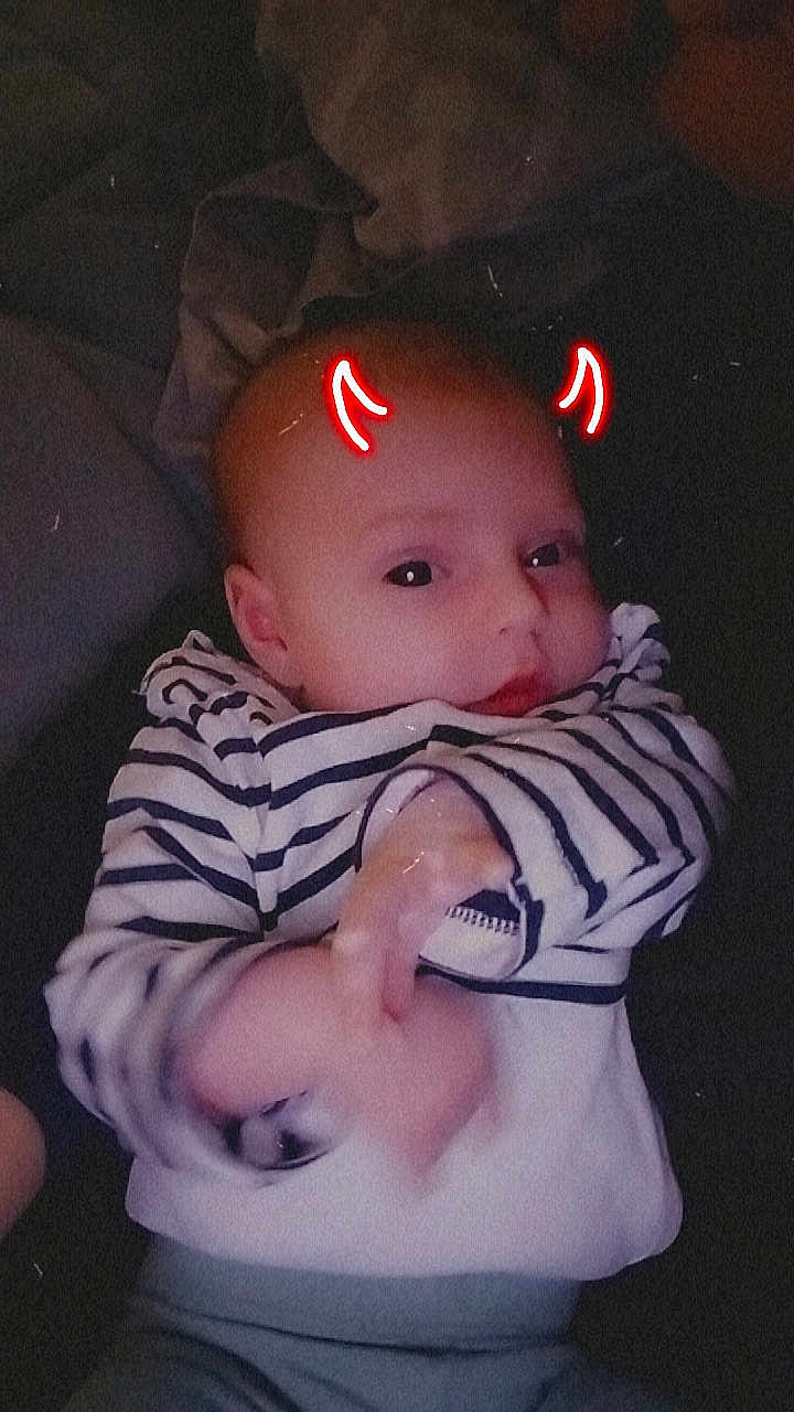 Céleste participe au concours pour gagner de l'argent avec cette photo : baby, infant, striped_clothing, lying_down, face, hand, red_horns, doodle, glow, cute, child, portrait, indoors, soft_light, expression, person, young_child, casual, head, skin