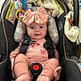 baby, car_seat, pink_clothing, headband, toy, blanket, smile, child, infant, safety_harness, cute, indoors, soft_toys, comfort, happy, seat, person, apparel, headwear, infant_clothing