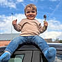 child, toddler, smiling, blue_sky, clouds, car_roof, jeans, socks, sweater, spoon, outdoor, happy, person, casual_clothing, daylight, playful, young_child, portrait, fun, sky