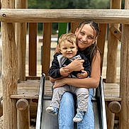 Lylio participe au concours pour gagner de l'argent avec cette photo : child, toddler, woman, slide, playground, wood, outdoor, smile, happy, casual_clothing, jeans, socks, embrace, nature, fun, family, park, daylight, person, play