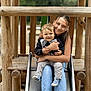 child, toddler, woman, slide, playground, wood, outdoor, smile, happy, casual_clothing, jeans, socks, embrace, nature, fun, family, park, daylight, person, play