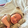 baby, newborn, knitted_clothing, bear_hat, crocheted_toy, teddy_bear, blanket, soft_texture, sleepy, infant, cute, portrait, resting, cozy, hand, face, indoors, warm, comfort, child