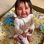 Nalani is registered to the contest to win money with this photo: baby, child, smiling, pajamas, playpen, toys, bottle, doll, floor, colorful, happy, infant, cute, indoors, sitting, playing, cheerful, face, hands, feet