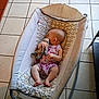 Kari is registered to the contest to win money with this photo: baby, sleeping, plush_toy, baby_rocker, tile_floor, infant, peaceful, indoor, child, furniture, footwear, patterned, resting, cute, one_person, relaxation, small_child, head, arm, leg