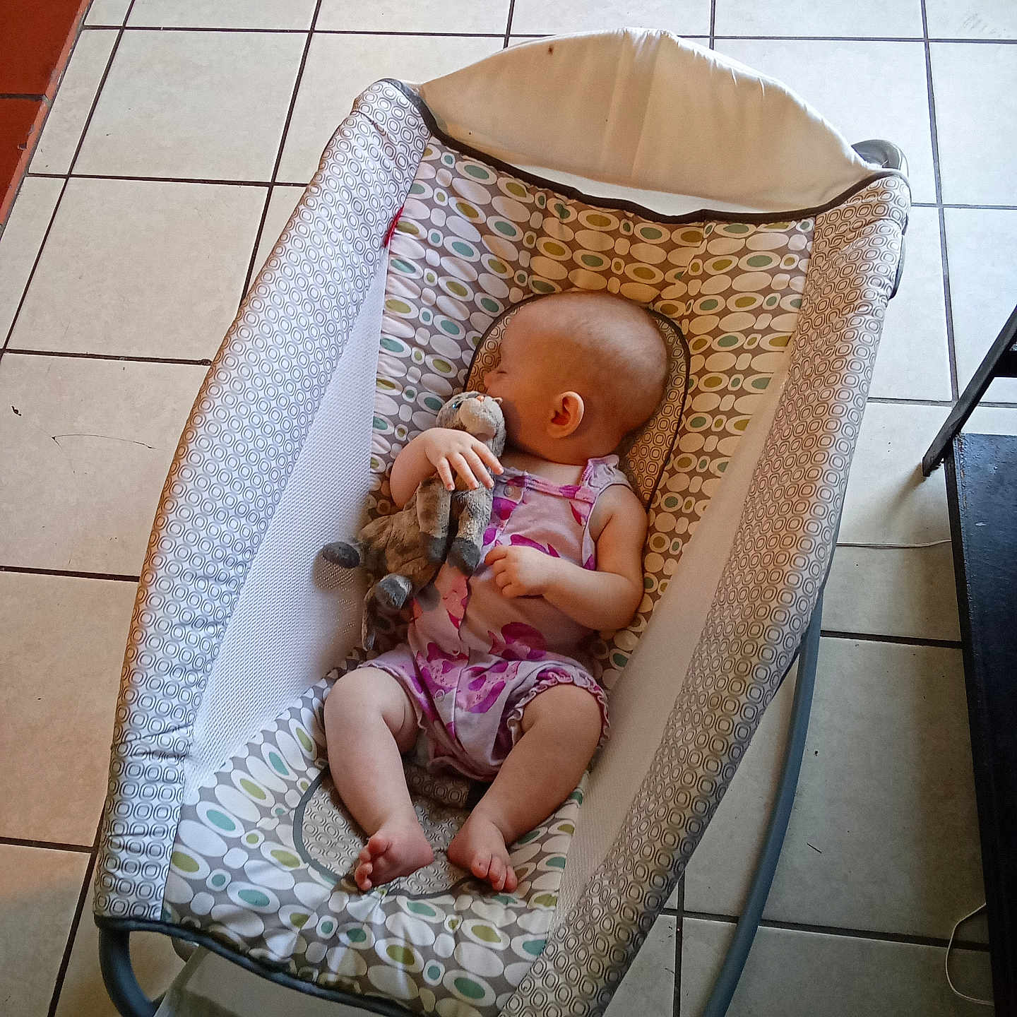 Kari is registered to the contest to win money with this photo: arm, baby, baby_rocker, child, cute, footwear, furniture, head, indoor, infant, leg, one_person, patterned, peaceful, plush_toy, relaxation, resting, sleeping, small_child, tile_floor