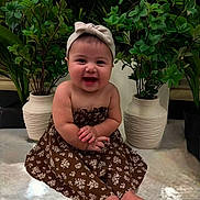 Leilani Funez is registered to the contest to win money with this photo: baby, barefoot, bow, child, cute, decor, dress, face, floor, floral_pattern, happy, indoor, infant, phone_screenshot, photograph, plants, portrait, potted_plants, sitting, smiling