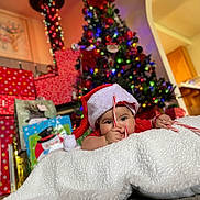 Daphne is registered to the contest to win money with this photo: baby, santa_hat, candy_cane, blanket, christmas_tree, gift_box, holiday, festive, indoors, decorations, colorful_lights, smiling, child, cute, celebration, holiday_season, present, home, christmas, cozy