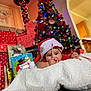 baby, santa_hat, candy_cane, blanket, christmas_tree, gift_box, holiday, festive, indoors, decorations, colorful_lights, smiling, child, cute, celebration, holiday_season, present, home, christmas, cozy