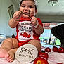 Daphne joined the competition — help win amazing prizes! baby, infant, red_onesie, tomato, tomato_vine, bracelet, headband, smile, indoor, blanket, dog, table, window, furniture, milestone, six_months, cute, chubby_cheeks, happy, person