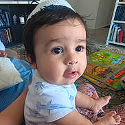Thiago joined the competition — help win amazing prizes! baby, child, infant, portrait, sitting, wide_eyed, dark_hair, white_shirt, barefoot, living_room, play_mat, bookshelf, books, television, rug, indoor, home, furniture, close_up, adorable