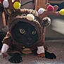 cat, black_cat, costume, reindeer_costume, antlers, pom_poms, carpet, indoor, pet, animal, cute, furry, yellow_eyes, claws, curious, crouching, soft_lighting, holiday, festive, playful