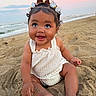 baby, child, sand, beach, sunset, smile, happy, cute, bow, hair_accessory, ocean, water, sky, outdoor, summer, toddler, sitting, clothing, infant, portrait