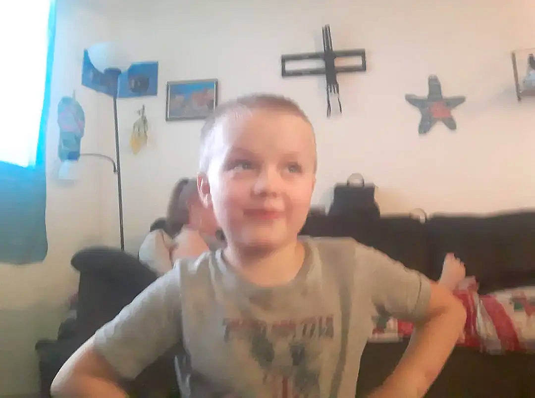 Devon is registered to the contest to win money with this photo: arm, chest, child, cross, elbow, event, finger, fun, gesture, happy, joy, mouth, person, religious_item, room, sleeve, smile, symbol, t_shirt, thumb