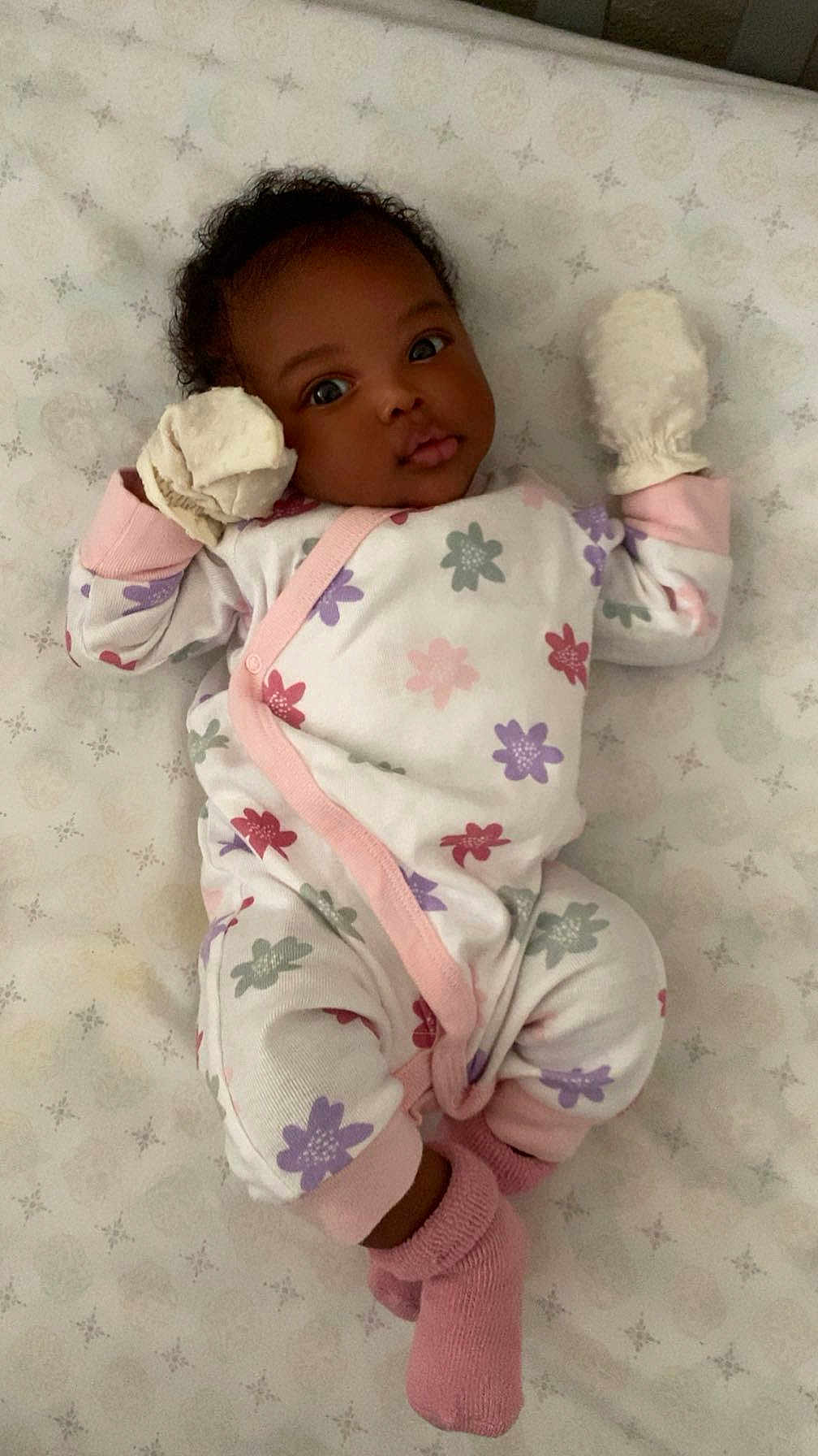 Avaia is registered to the contest to win money with this photo: baby, infant, onesie, mittens, socks, lying_down, bed, mattress, pattern, floral, cute, child, newborn, sleepwear, pink, white, purple, red, face, portrait