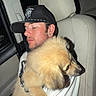 man, dog, car_interior, cap, tattoo, white_shirt, fluffy_dog, closed_eyes, light_brown_dog, headrest, seat, night, portrait, pet, hug, calm, intimate, side_view, human, animal