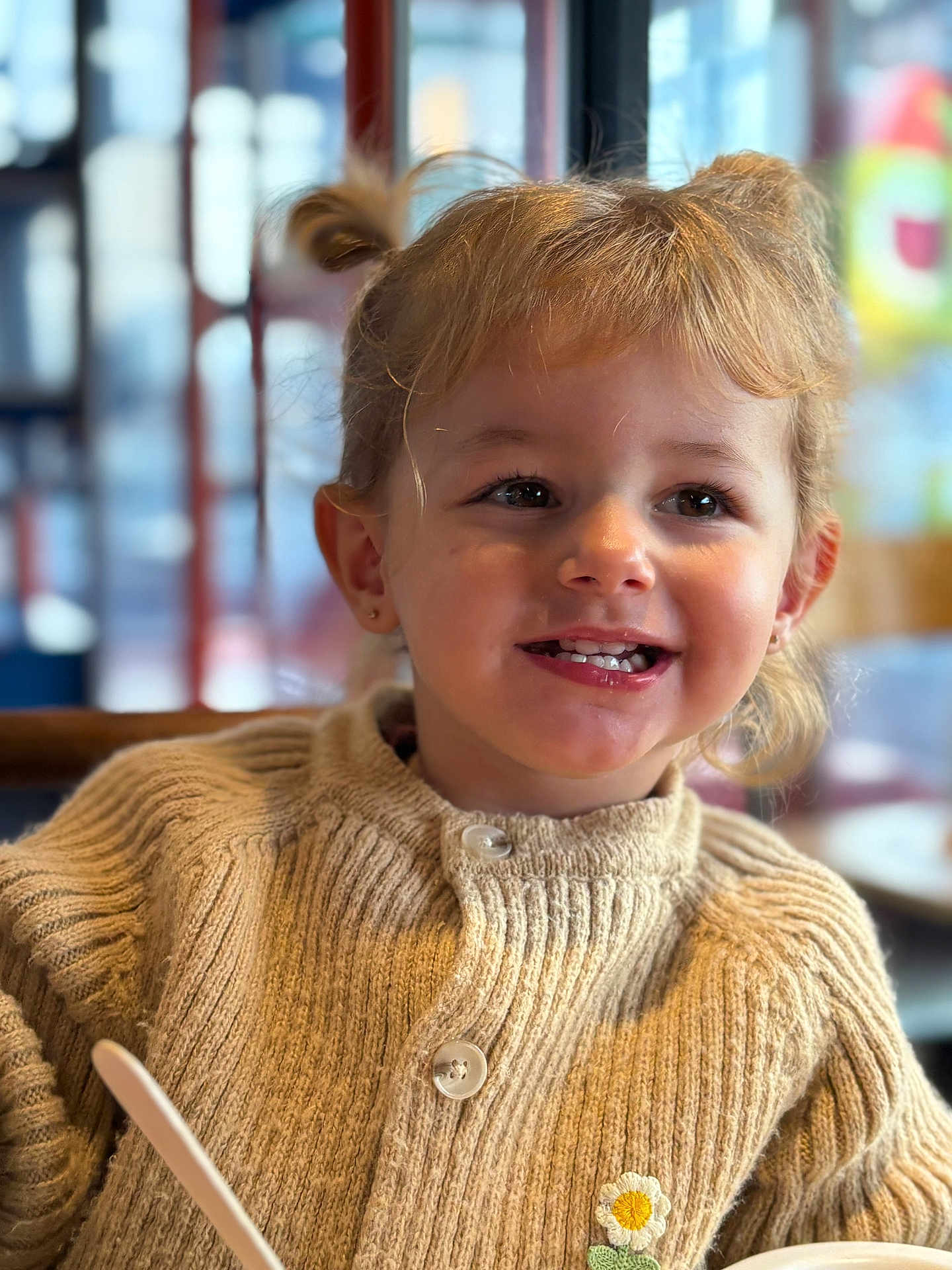 Lyna a rejoint le concours — aidez-le/la à gagner de superbes lots ! bokeh, bowl, buttons, child, daisy_patch, earrings, eating, girl, hair, indoor, knitwear, pigtails, portrait, restaurant, smile, spoon, sweater, table, teeth, toddler