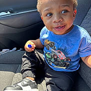 Drayden is registered to the contest to win money with this photo: black_pants, blue_tshirt, car_interior, car_seat, casual_clothing, child, curious_expression, curly_hair, cute, daylight, holding_object, indoors, monster_truck, portrait, seatbelt, sitting, smiling, sneakers, toddler, young_child