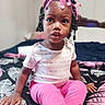 Mya joined the competition — help win amazing prizes! toddler, child, girl, pink_pants, pink_bow, headband, braided_hair, patterned_blanket, bedroom, indoor, sitting, curious, clothing, person, young_child, portrait, expression, hand, furniture, casual
