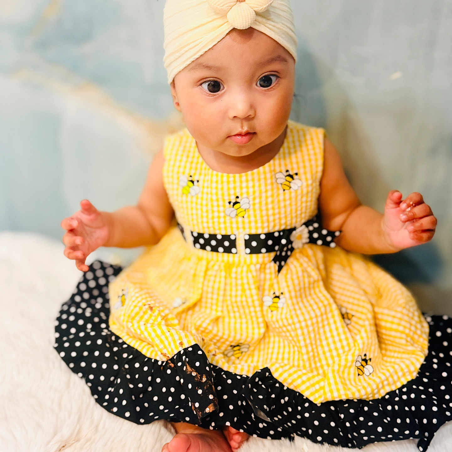 Mia joined the competition — help win amazing prizes! baby, child, infant, dress, yellow_dress, headband, flower_headband, polka_dot, sitting, barefoot, curious, cute, indoors, soft_background, fluffy_surface, portrait, hands, feet, smiling, closeup