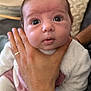 baby, infant, newborn, face, wide_eyes, hand, adult_hand, ring, onesie, blanket, pillow, couch, close_up, portrait, indoors, soft_texture, gaze, eyelashes, support, cozy