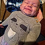 Dakota is registered to the contest to win money with this photo: baby, smile, sweater, knitted, raccoon_design, dimple, hand, blanket, person, infant, clothing, cute, happy, portrait, indoor, warm, resting, comfort, face, head
