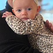 Dakota joined the competition — help win amazing prizes! baby, infant, headband, flower, leopard_print, onesie, person, holding, black_sweater, closeup, face, eyes, cute, soft_focus, indoor, portrait, child, young, hand, apparel