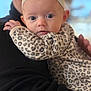 baby, infant, headband, flower, leopard_print, onesie, person, holding, black_sweater, closeup, face, eyes, cute, soft_focus, indoor, portrait, child, young, hand, apparel