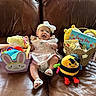 baby, infant, smile, dress, headband, bow, toy, plush, bee, basket, book, couch, leather, child, cute, indoors, happy, sitting, playful, colorful