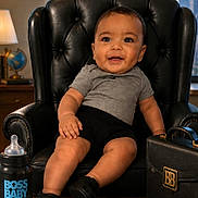 Liam joined the competition — help win amazing prizes! baby, child, chair, leather_chair, briefcase, bottle, nameplate, smiling, indoors, window, cityscape, business, office, cute, portrait, person, black_clothing, gray_shirt, desk, happy
