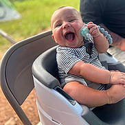 Sylas joined the competition — help win amazing prizes! baby, high_chair, pacifier, striped_clothing, outdoor, greenery, happy, laughing, child, person, infant, seat, smile, holding, arm, casual_clothing, blurred_background, sunlight, cheerful, playful
