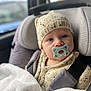 baby, child, pacifier, knitted_hat, knitted_sweater, car_seat, blanket, seatbelt, blue_eyes, indoor, portrait, infant, cute, warm_clothing, car_interior, young_child, face, person, sitting, cozy
