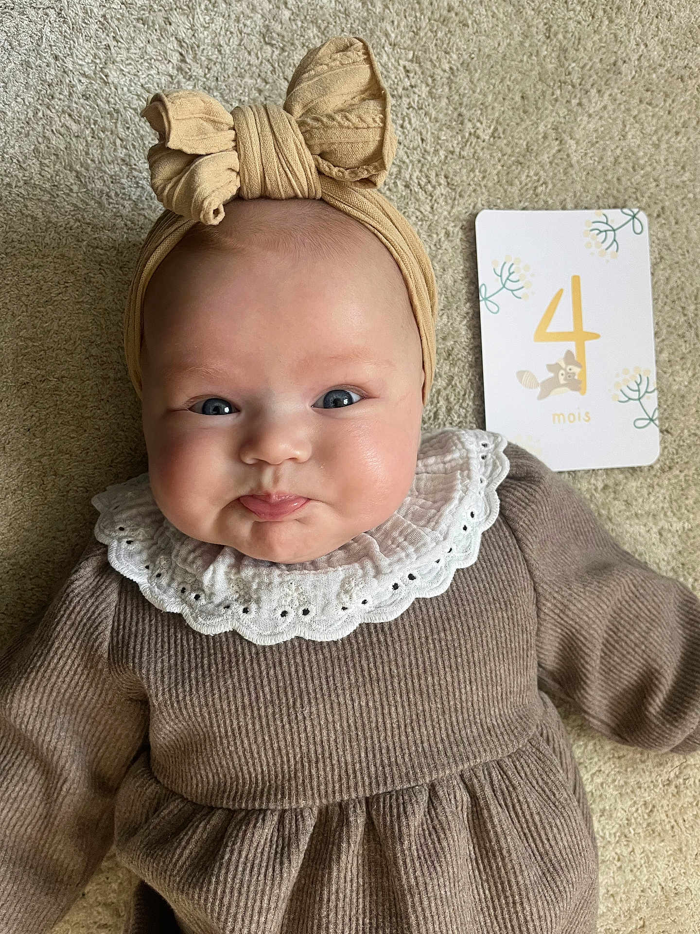 Victoria participe au concours pour gagner de l'argent avec cette photo : baby, infant, headband, bow, pouty_face, milestone_card, 4_months, carpet, soft_texture, clothing, neutral_colors, cute, portrait, child, young_baby, indoors, close_up, smiling_eyes, white_collar, lying_down