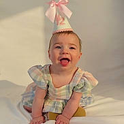 Miley joined the competition — help win amazing prizes! baby, child, smiling, party_hat, pink_bow, dress, pastel_colors, sitting, happy, indoor, portrait, cute, infant, young_child, face, skin, hands, playful, celebration, light_shadow