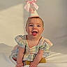 baby, child, smiling, party_hat, pink_bow, dress, pastel_colors, sitting, happy, indoor, portrait, cute, infant, young_child, face, skin, hands, playful, celebration, light_shadow