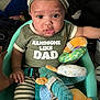 baby, infant, child, person, baby_seat, plush_toy, striped_hat, striped_pants, green_shirt, text_on_shirt, hand, indoors, curious_expression, sitting, safety_belt, cute, closeup, soft_toys, home, portrait