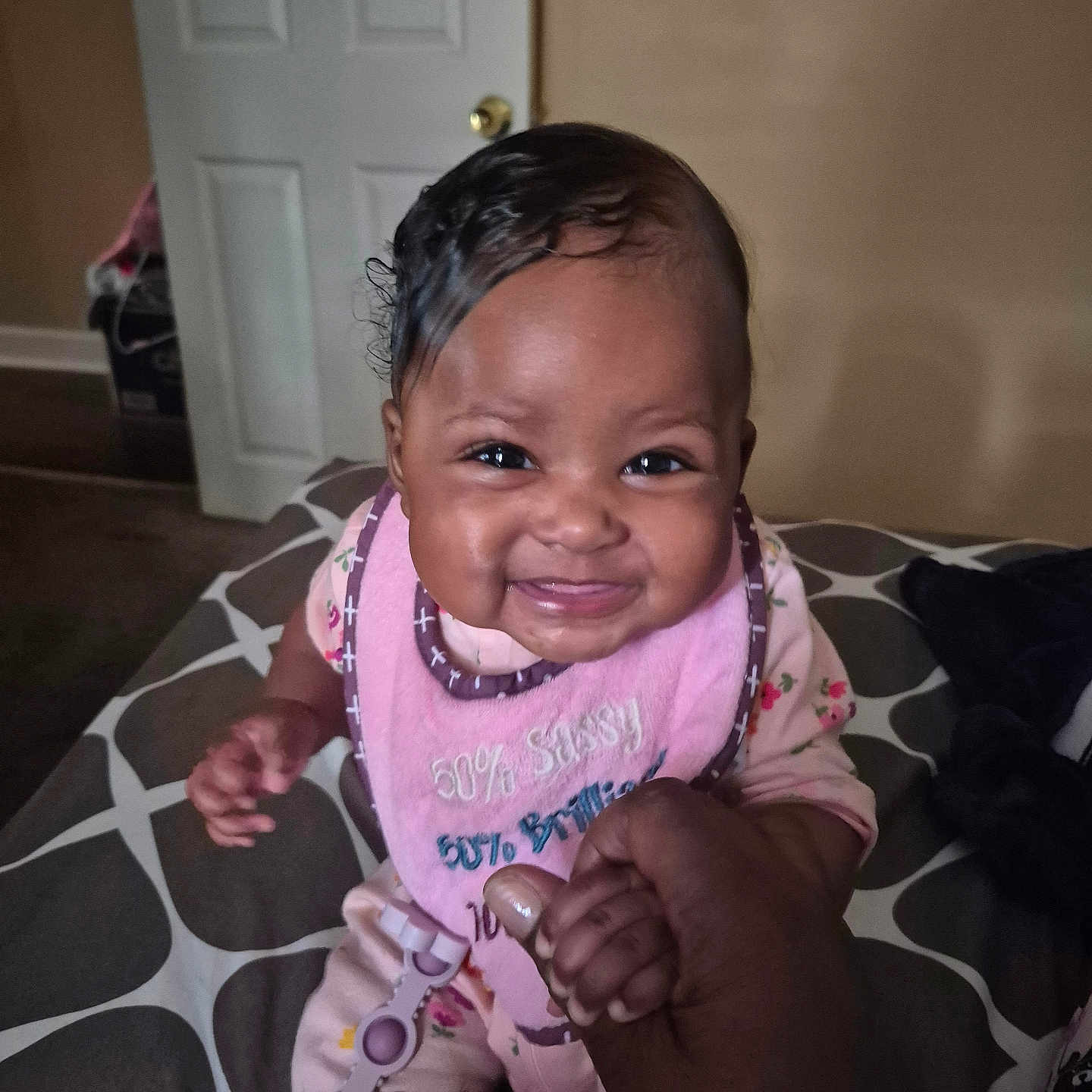Ariyana is registered to the contest to win money with this photo: baby, bed, bib, clothing, cute, door, face, fingertip, hair, hand, happy, holding, indoor, infant, pattern, person, pink, room, smiling, toy