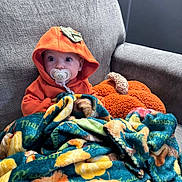 Lucas joined the competition — help win amazing prizes! baby, blanket, child, colorful_blanket, couch, cozy, cute, expression, face, home, hoodie, indoor, infant, orange_clothing, pacifier, plush_pillow, pumpkin, sitting, sofa, warm