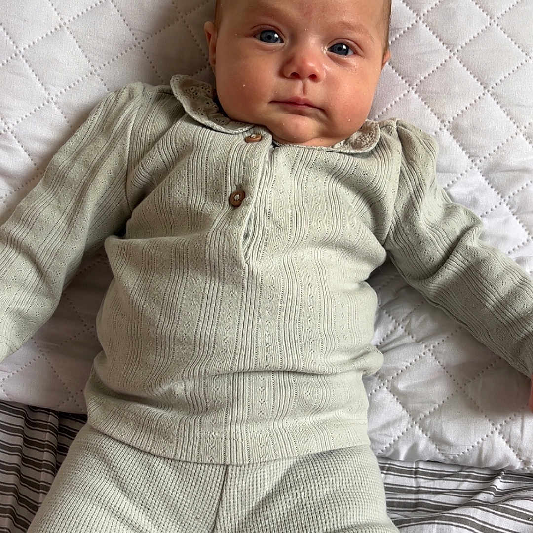 Lorïana a rejoint le concours — aidez-le/la à gagner de superbes lots ! baby, bed, blue_eyes, calm, child, clothing, comfortable, cute, face, home, indoor, infant, knitwear, lying_down, person, pillow, portrait, quilted_pillow, soft_texture, striped_bedding
