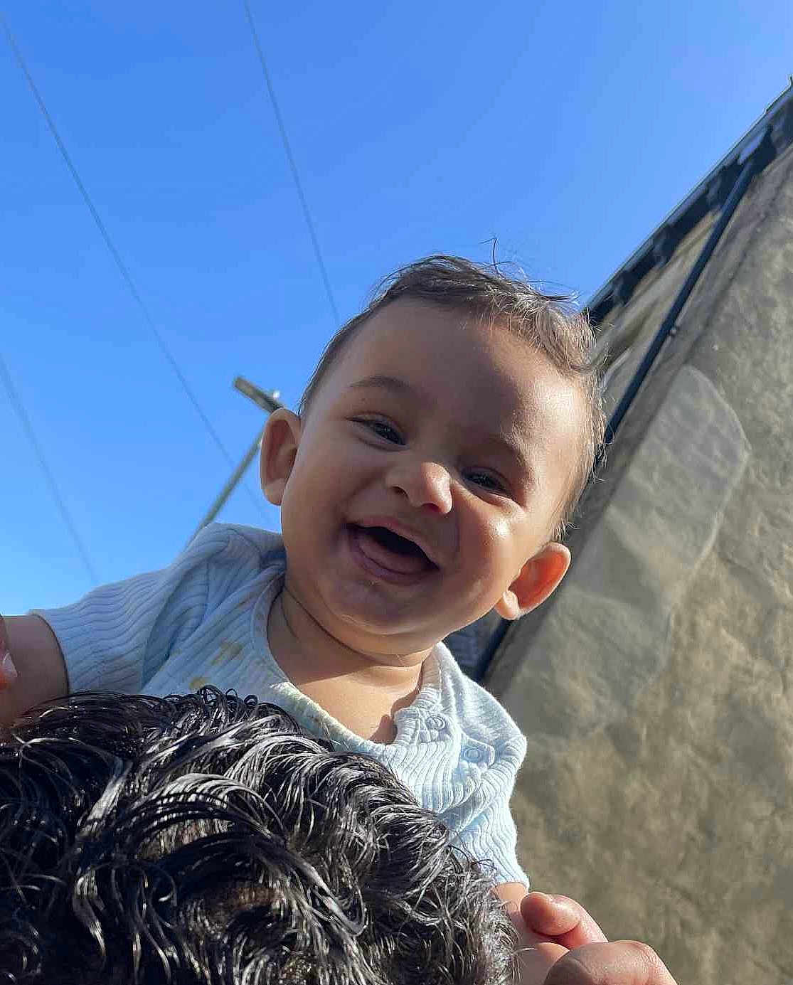 Raymon joined the competition — help win amazing prizes! baby, child, smiling, happy, outdoor, blue_sky, person, face, head, hair, curly_hair, clothing, light, sunlight, holding, joy, portrait, infant, cute, playful